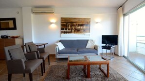 Ein Wohnzimmer mit grauem Sofa, zwei Sesseln, einem Couchtisch und einem Fernseher auf einem Schrank.