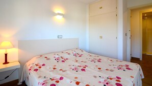 Ein Schlafzimmer mit einem Bett, einem Nachttisch mit Lampe, einem Kleiderschrank und einer Wandleuchte.
