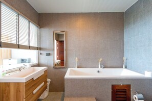 A modern bathroom with a large sink, mirror, and bathtub.