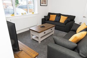 Una sala de estar con un sofá gris, una mesa de centro de madera y un televisor sobre un mueble.