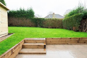 Un jardin avec une terrasse en bois, une pelouse et une haie.