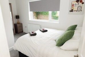 Un dormitorio con cama, ventana, radiador, mesita de noche y lámpara.
