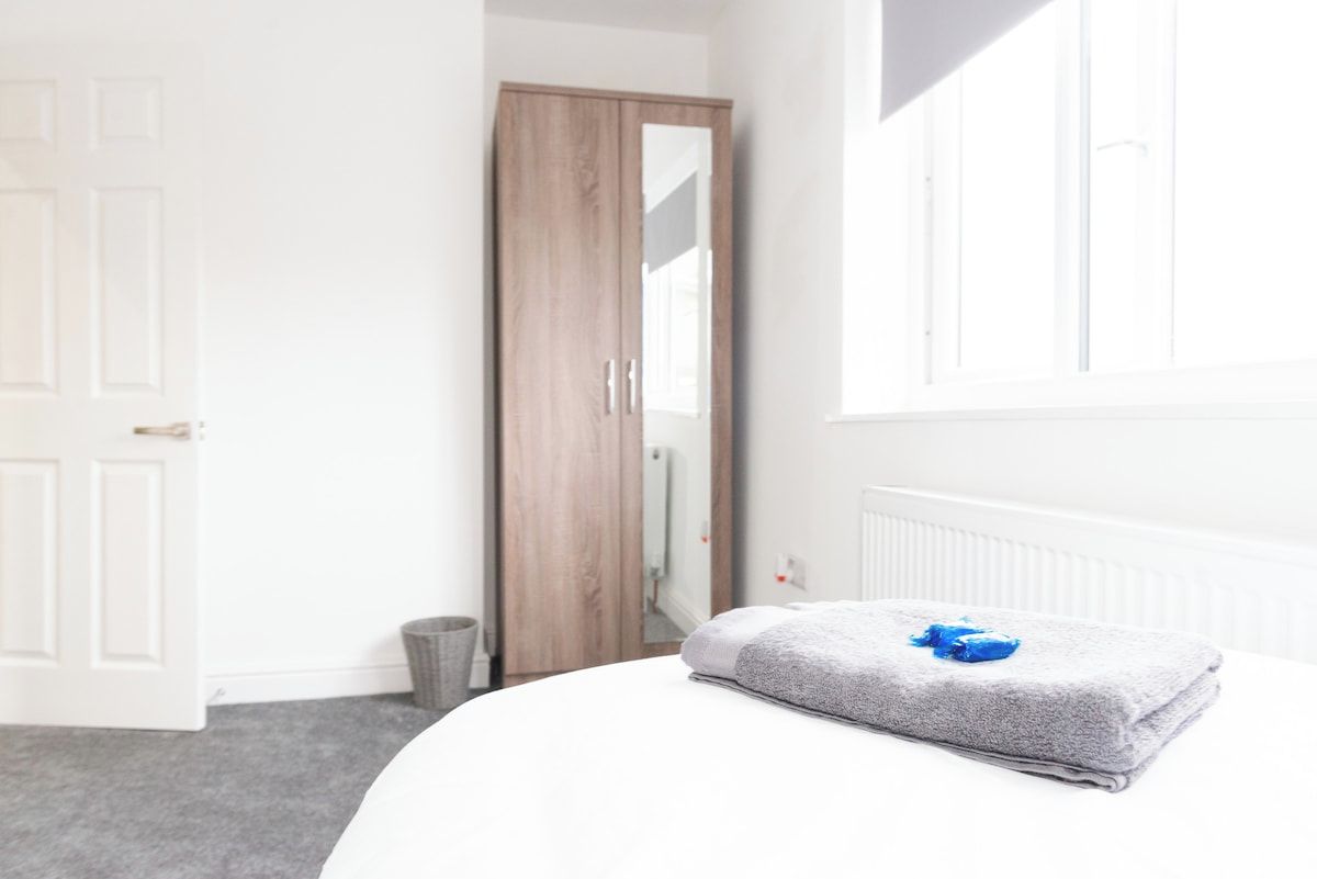 A bedroom with a bed, a grey towel with a blue object, a wooden wardrobe, and a white radiator.