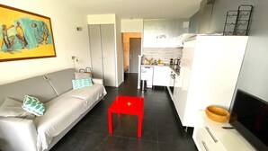 A modern apartment with a living room, a red coffee table, a grey sofa, a kitchen, and a dining area. - "L'Océane" Studio sea view-climate-wifi-parking (La Ciotat)
