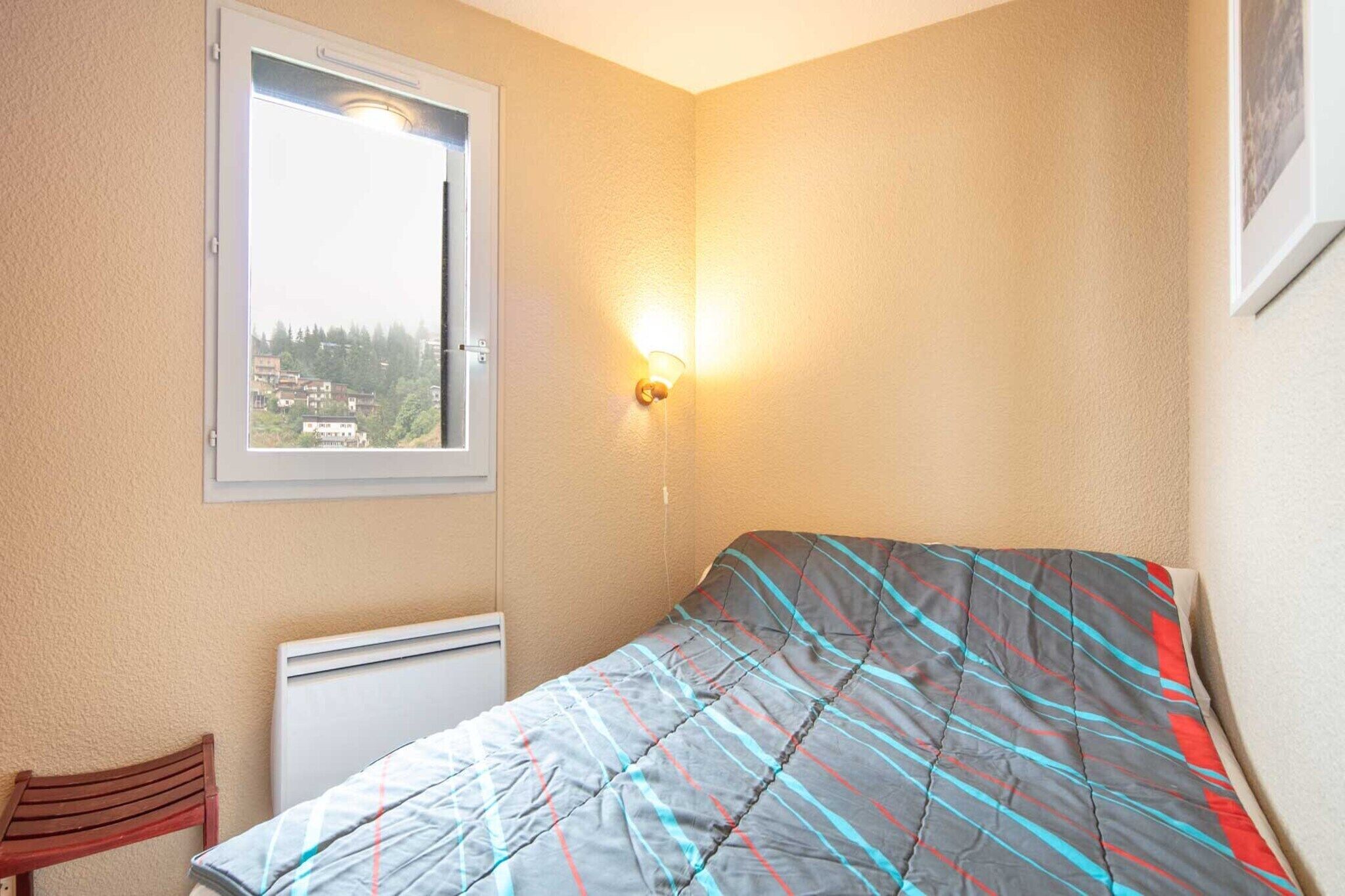 Et soveværelse med seng, et vindue, en radiator og en lampe på væggen.
