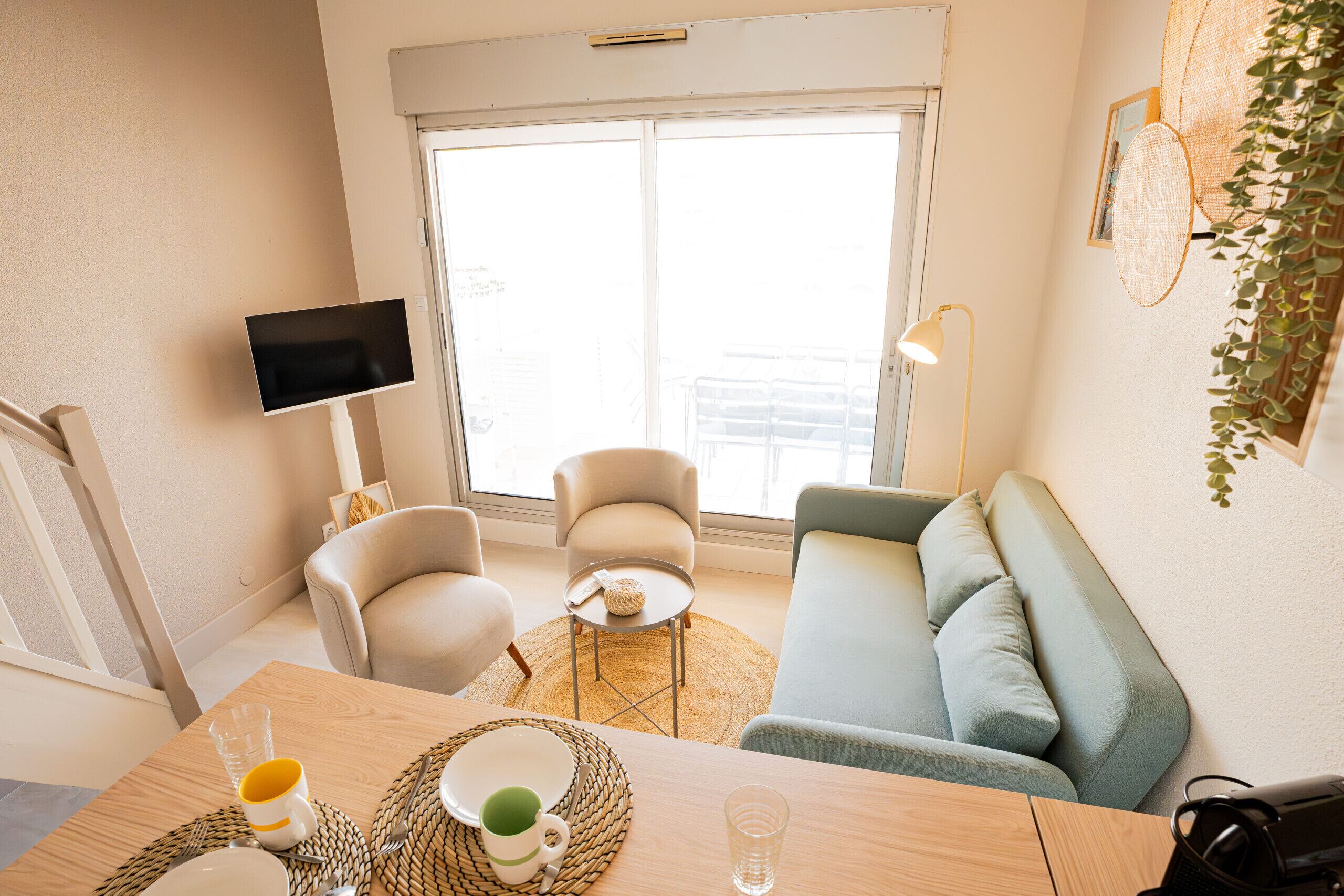 Una sala de estar moderna con sofá, sillones, una mesa de comedor y un televisor, junto a un amplio ventanal.