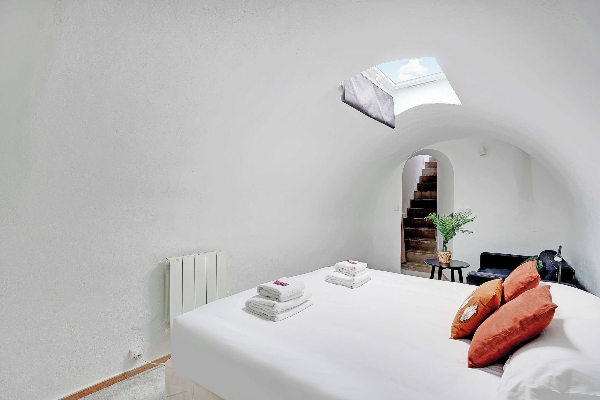 Quarto de hotel com cama, toalhas brancas, uma mesinha com uma planta e vista para uma escadaria.