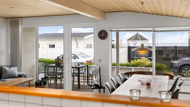 Une cuisine moderne avec un plafond en bois, un coin repas avec une longue table et des chaises, et une vue sur le jardin à travers de grandes fenêtres.