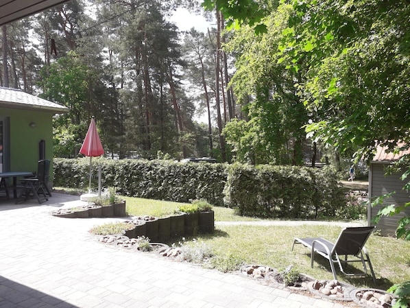 A patio area with a table and chairs, a red umbrella, and a bench.