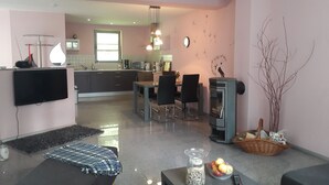 A modern living room with a flat-screen TV, a dining area with chairs, a kitchen in the background, and a fireplace. - Interesting vacation home by the lake and forest, Uckermark, Lychen the town of 7 lakes (Lychen)