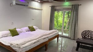 Un dormitorio con cama, escritorio y vistas a la vegetación a través de un ventanal.