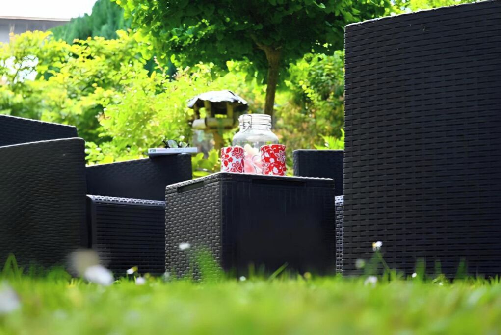 Mobilier en osier pour l’extérieur, avec une bouteille en verre et un gobelet rouge et blanc.