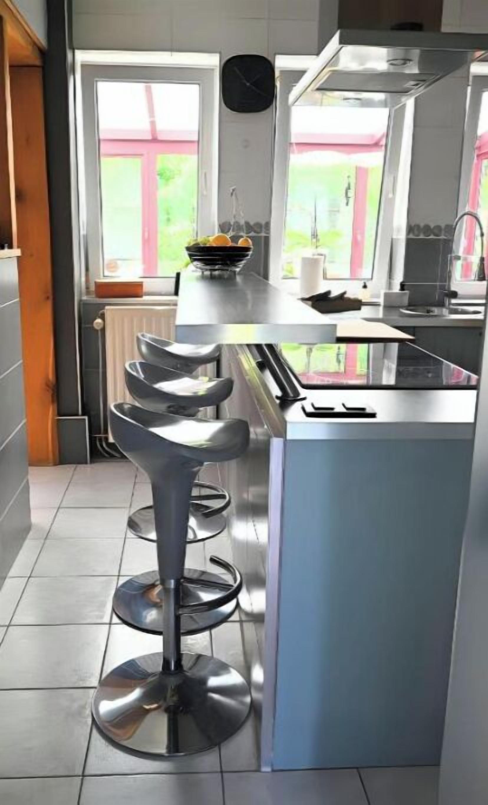 Een moderne keuken met een centraal eiland, roestvrijstalen apparatuur en een raam met uitzicht op groen.