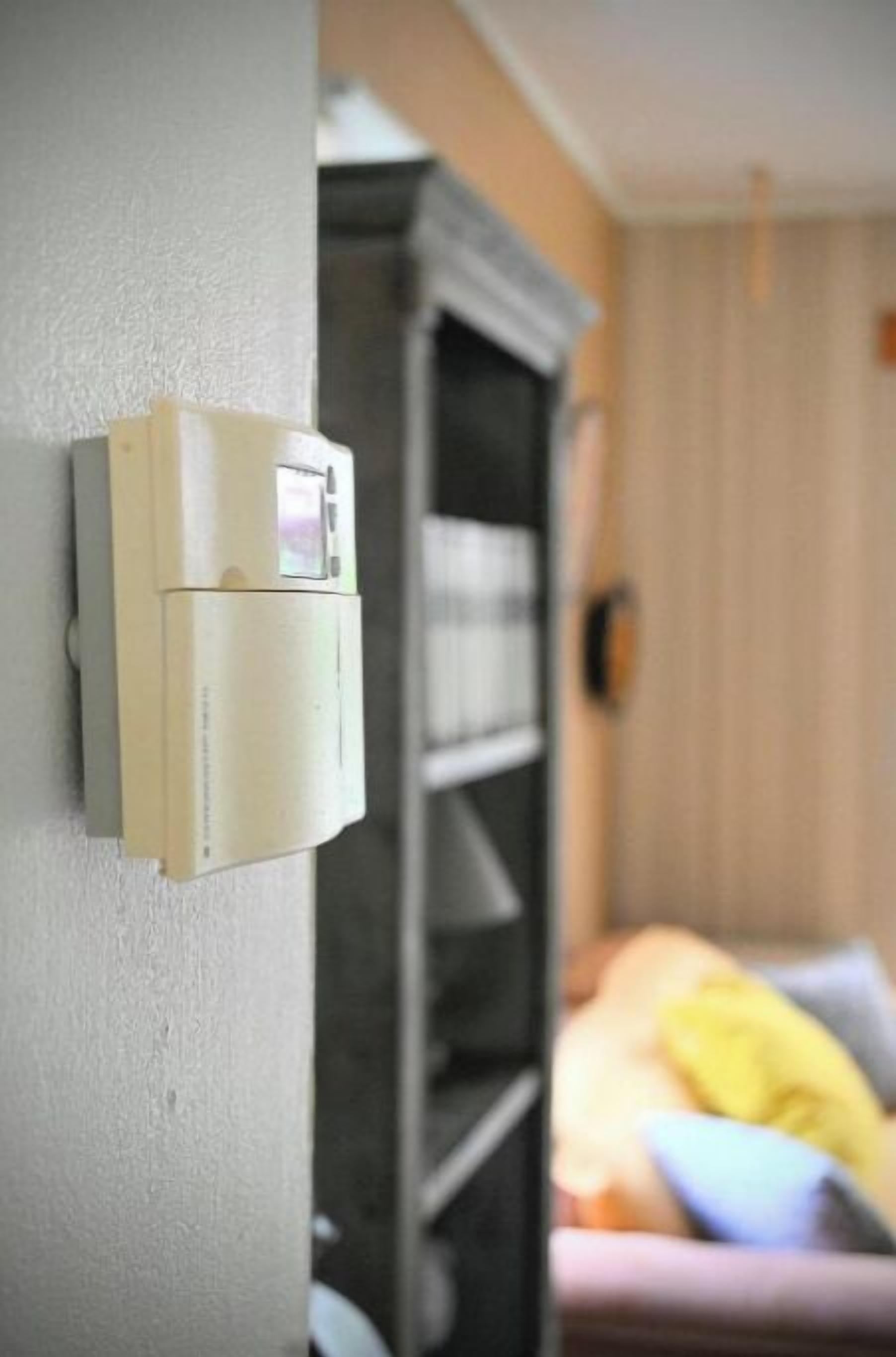 Un termostato en la pared, una estantería y una cama con almohadas.