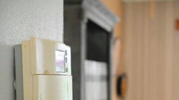 Un termostato en la pared, una estantería y una cama con almohadas.