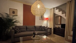 Ein Wohnzimmer mit einer Couch, einem Glastisch, einer Pendelleuchte, einer roten Lampe und einem gerahmten Bild an der Wand.