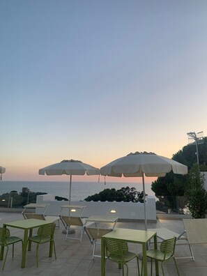 An outdoor seating area with tables and chairs, large umbrellas, and a view of the sea at sunset. - Relais Ulivo Ariana (Gaeta)