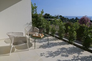 A balcony with two wicker chairs, a small table with a tray of items, and a view of the sea and greenery. - Relais Ulivo Ariana (Gaeta)