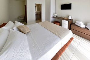 A hotel room with a large bed, a desk with a lamp, a TV, and a bathroom visible through an open door. - Relais Ulivo Ariana (Gaeta)