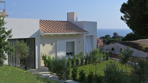 Una casa moderna con techo de tejas, fachada blanca y vista al mar.