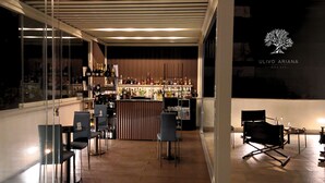 Zona de bar moderna con mostrador de madera, estanterías llenas de botellas y un espacio de estar con sillas.
