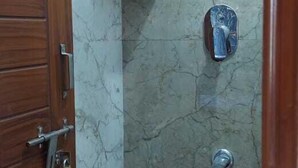 A small bathroom with a shower, a wooden door, and a brown bucket. - SGR Paradise (Bengaluru)