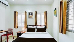 A hotel room with a bed, a desk, a chair, and two windows with curtains. - SGR Paradise (Bengaluru)
