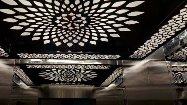 An interior with a patterned ceiling design, metallic walls, and a central column. - SGR Paradise (Bengaluru)