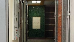 A hallway with a tiled floor, a green wall with a decorative element, and a door with a metal handle. - SGR Paradise (Bengaluru)