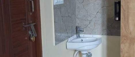 A bathroom with a wooden door, a sink, a mirror, and a marble wall.
