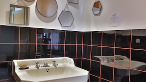 A bathroom with a white pedestal sink, black and red tiled walls, and geometric wall decorations. - Room POP - Private bathroom (Montbron)