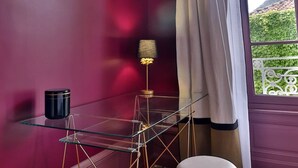 Una habitación con una mesa de vidrio, un taburete pequeño y una lámpara frente a una pared morada.