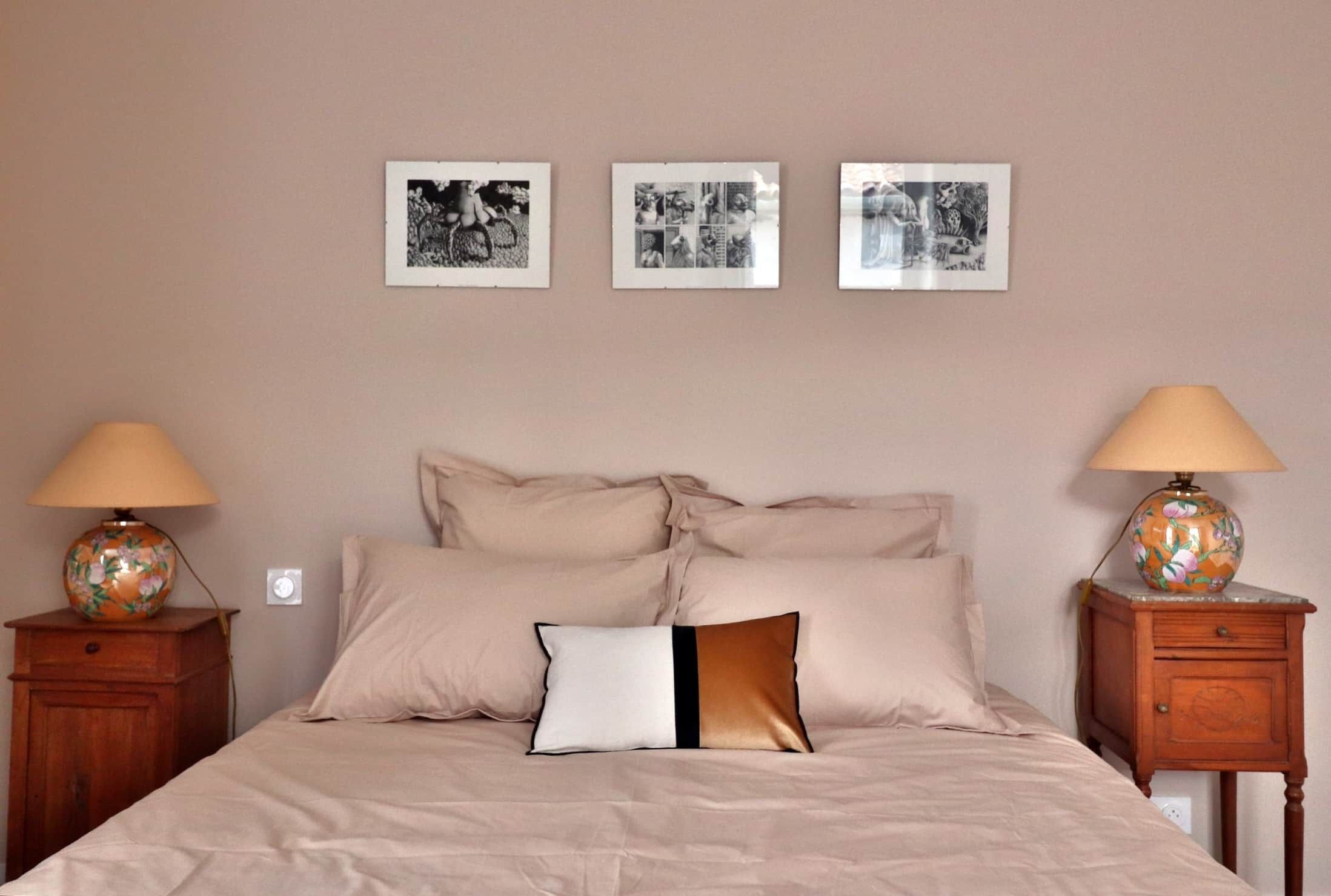 A bedroom with a bed, two nightstands, and three framed pictures on the wall.