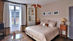 Ein Schlafzimmer mit einem Bett, einem Deckenventilator, einem Fernseher, einem kleinen Tisch, einer Lampe und einer Tür.