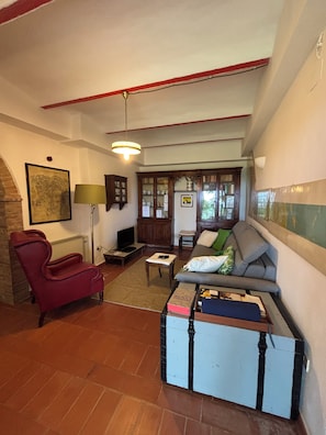 A living room with a red armchair, a sofa, a small table, and a cabinet. - IL PIETRAIO Guardistallo, a historic farmhouse surrounded by greenery (Guardistallo)