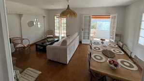 A spacious living area with a sofa, a dining table with placemats, and a wicker chair.