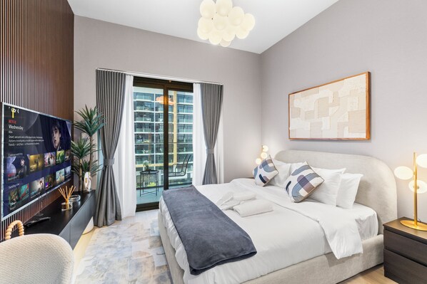 A modern hotel room with a large bed, a television displaying a Netflix interface, a view of the cityscape through the window, and a framed artwork on the wall. - Luxury Apartments in Meydan (Dubai)