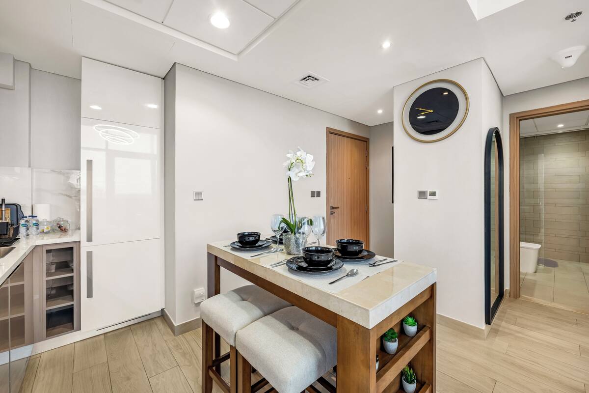 A modern kitchen with white cabinetry, a wooden dining table set with black dishes, and a potted orchid.