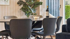 A dining area with a table, chairs, a potted plant, a wine bottle, and a glass.