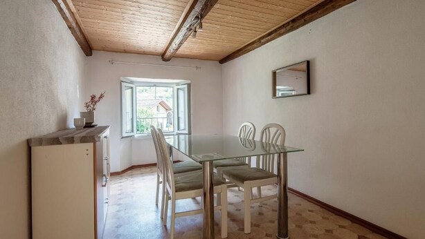 Uma área de refeições com mesa e cadeiras de vidro, um armário branco e uma janela com vista.
