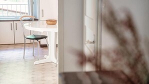 Uma cozinha com mesa e cadeira brancas, uma janela e uma tigela sobre a mesa.