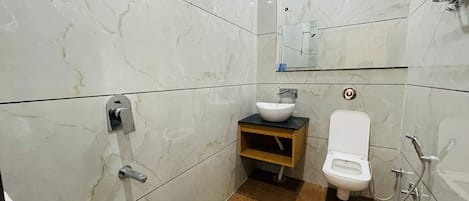 A bathroom with white marble tiles, a wooden vanity, a white toilet, and a glass-enclosed shower area.