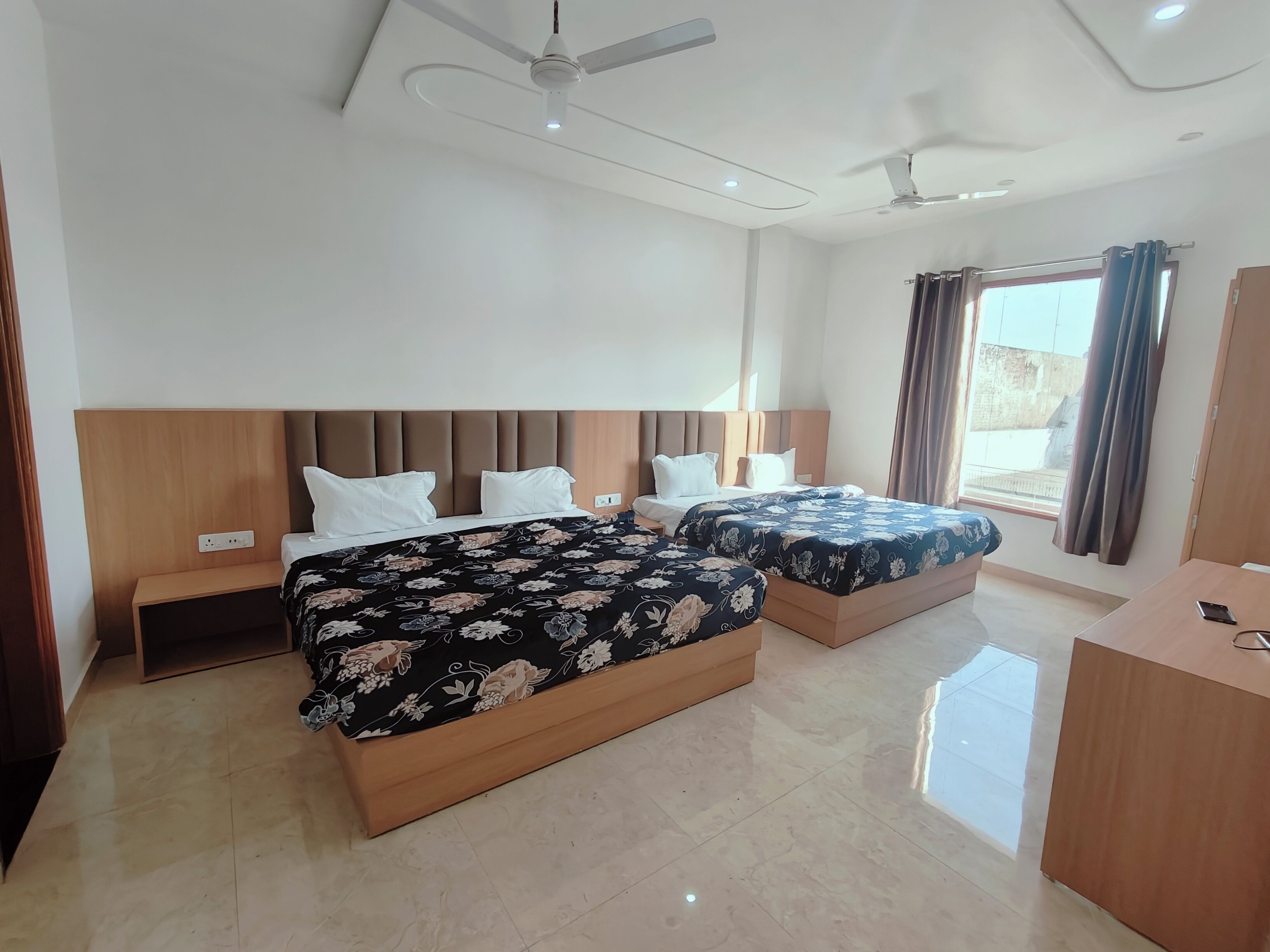 A hotel room with two beds, a wooden headboard, a desk, and a ceiling fan.