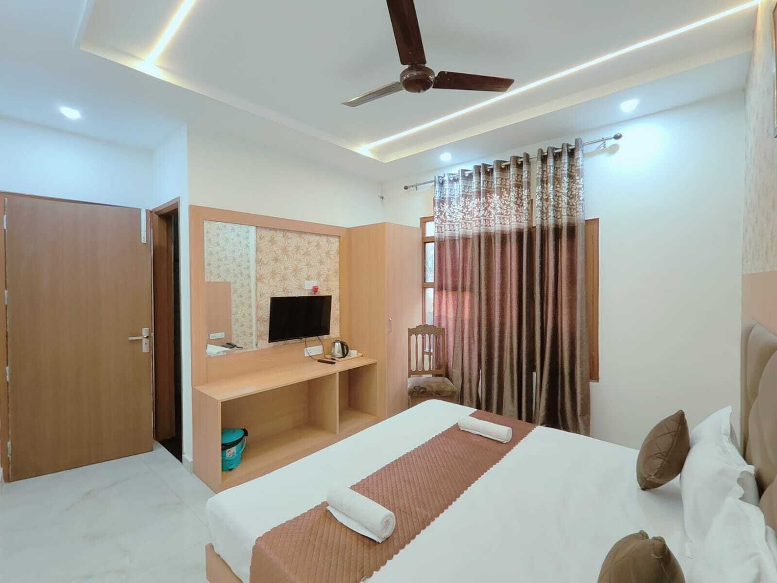 A hotel room with a bed, a desk, a television, a ceiling fan, and a window with curtains.