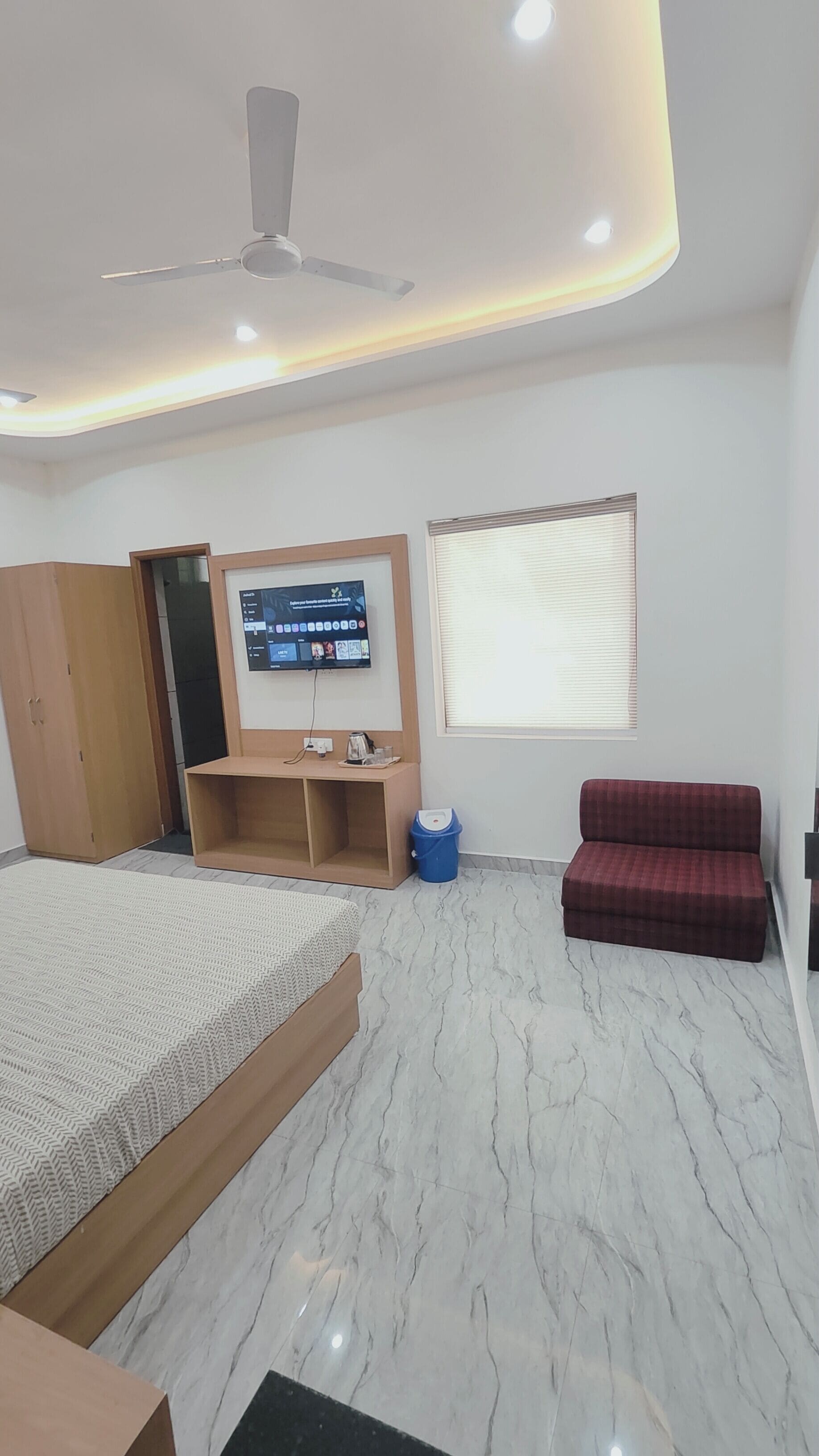 A modern bedroom with a bed, a TV, a red sofa, a wooden cabinet, and a ceiling fan.