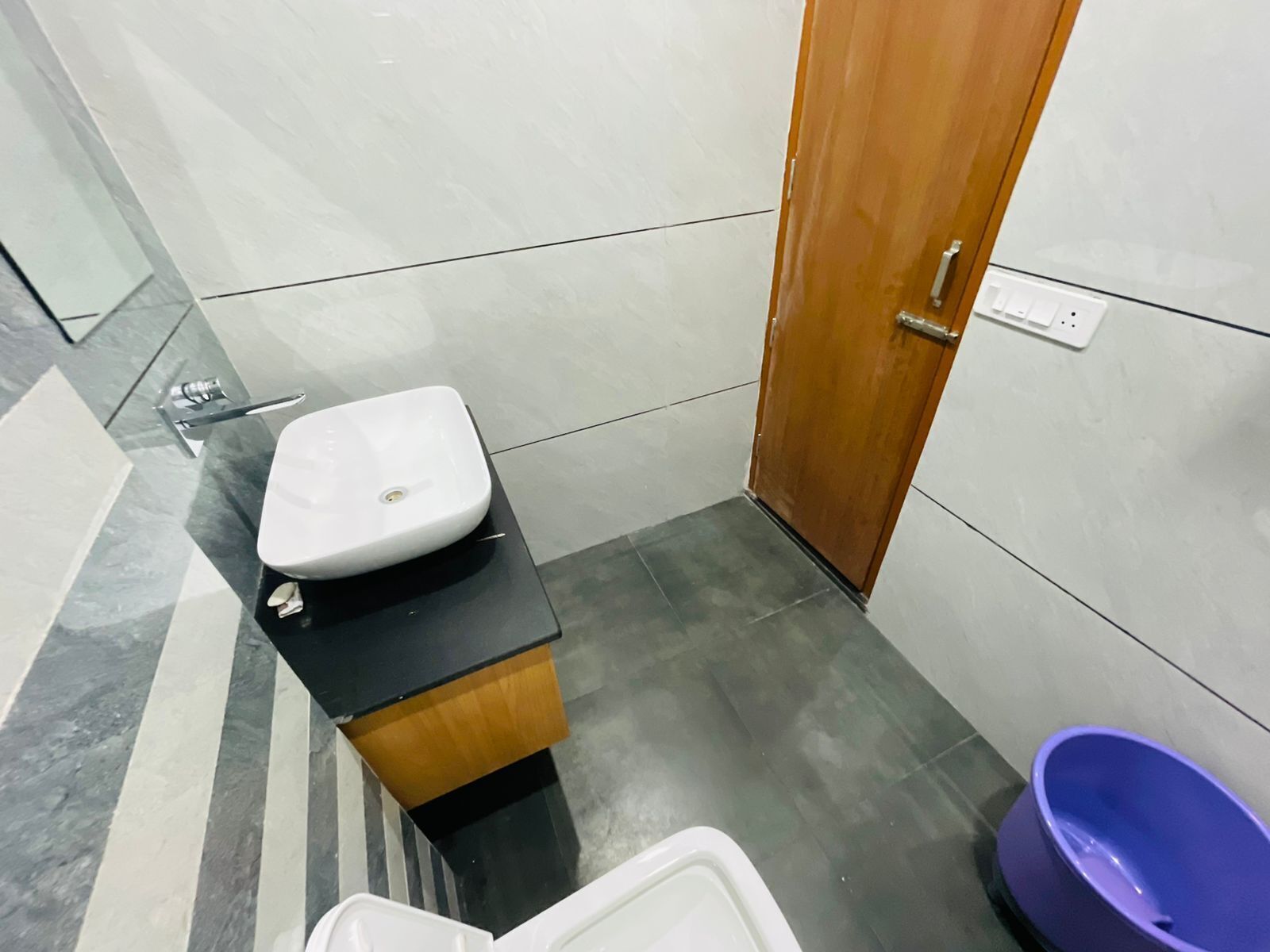 A small bathroom with a white sink, a wooden cabinet, and a purple basin.
