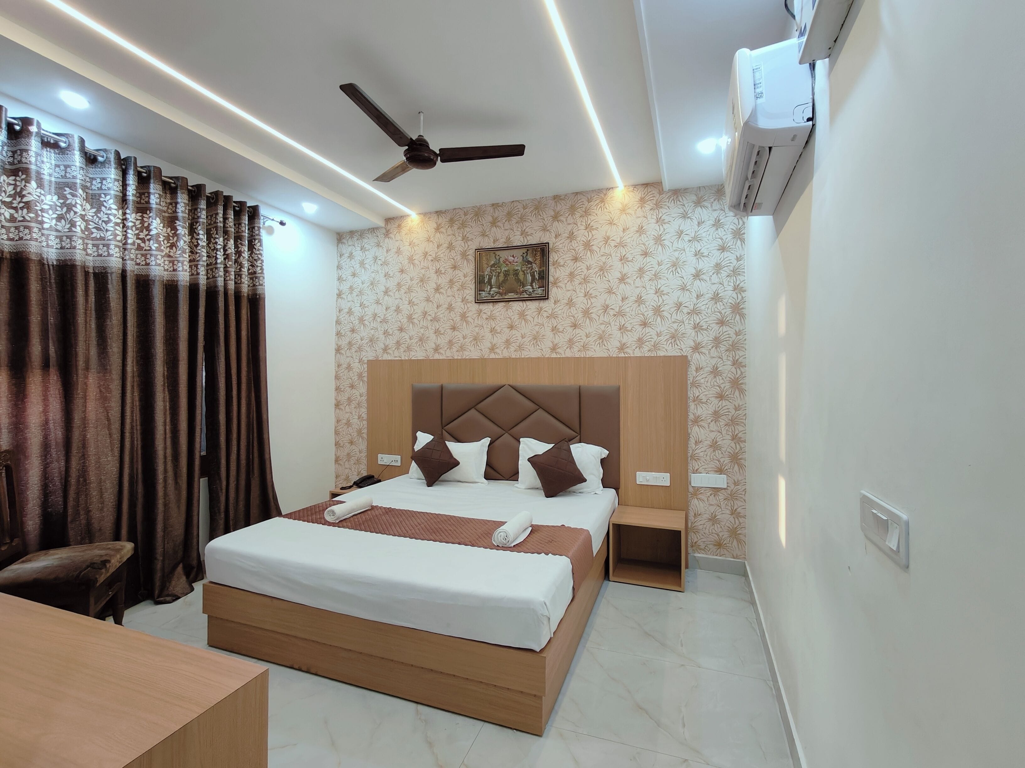 A hotel room with a bed, bedside tables, a ceiling fan, an air conditioning unit, and a patterned wallpaper.