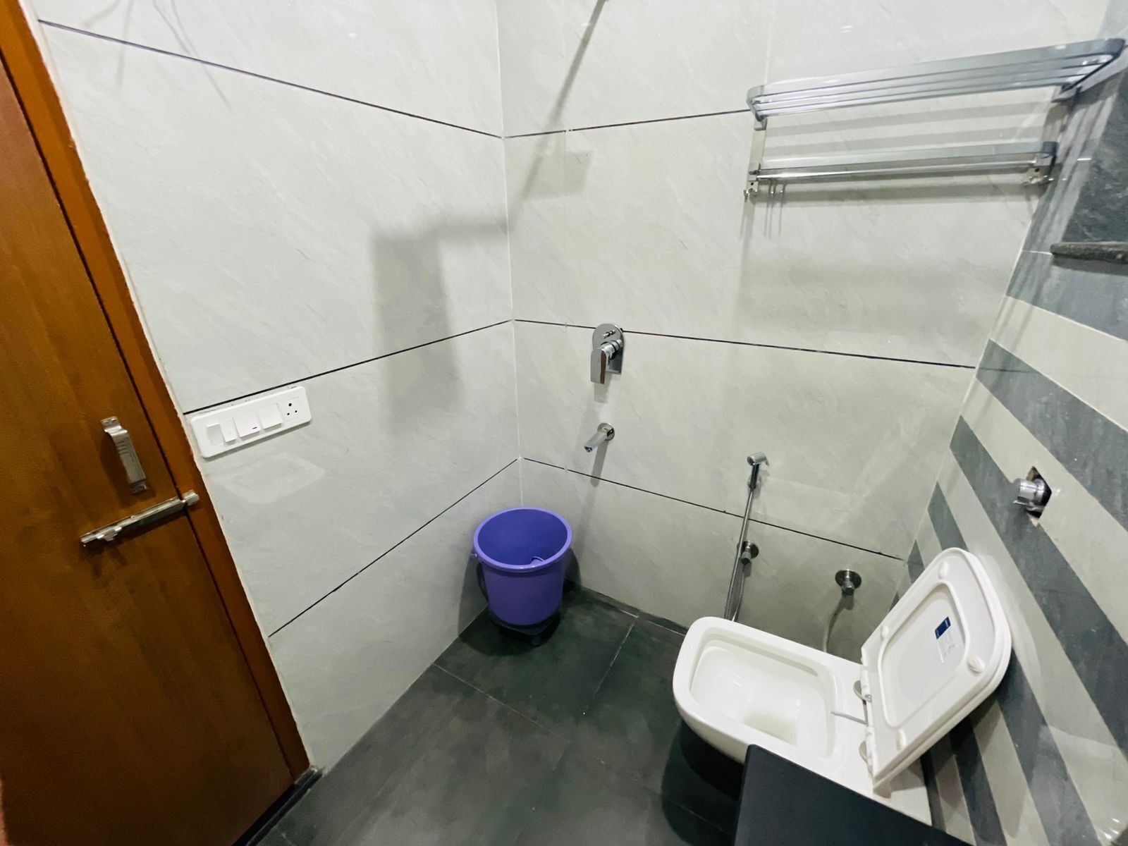 A small, tiled bathroom with a toilet, bidet, and a blue bucket.