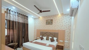 A hotel room with a large bed, a ceiling fan, an air conditioning unit, a desk, and a chair. - Hotel Pilgrim Near Golden Temple (Amritsar)