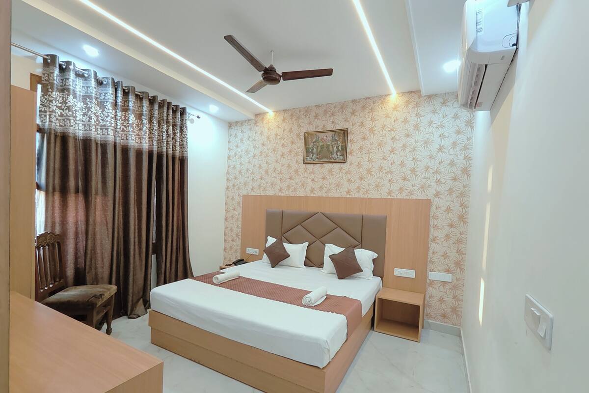 A hotel room with a large bed, a ceiling fan, an air conditioning unit, a desk, and a chair.